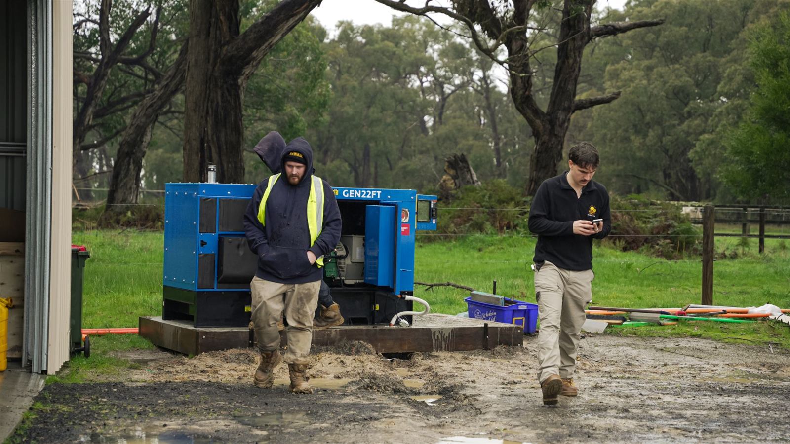 Two Sunsave crew members walking away from a newly installed generator on a muddy rural site