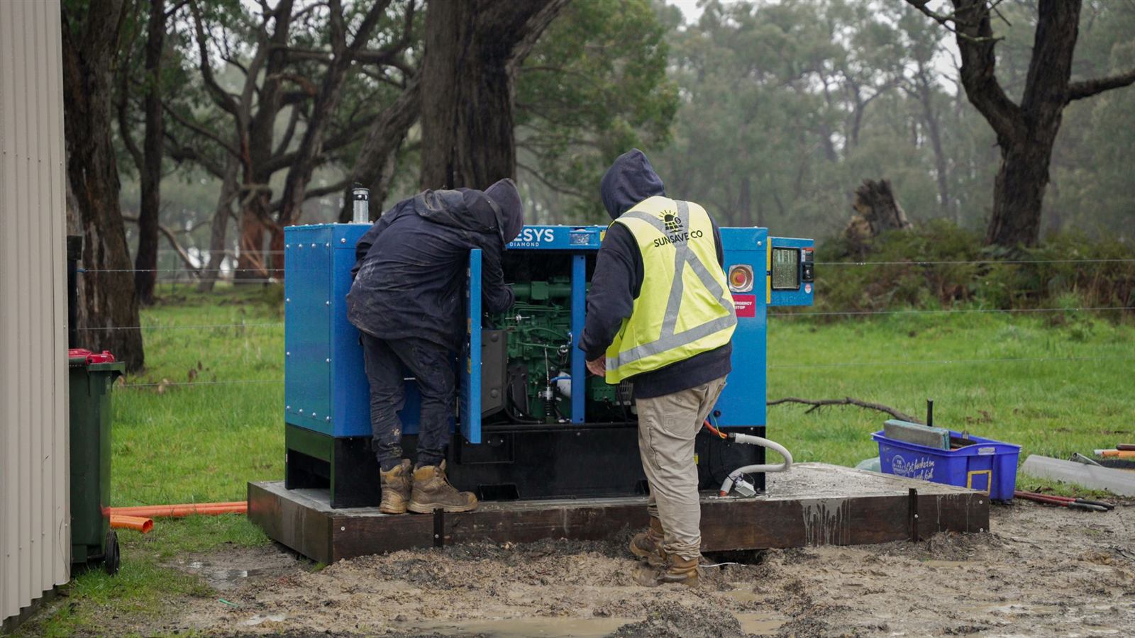 Two Sunsave crew members working inside an open generator enclosure on a rural property